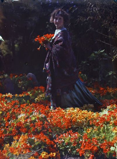 an old photo of a woman standing in a field full of orange and yellow flowers