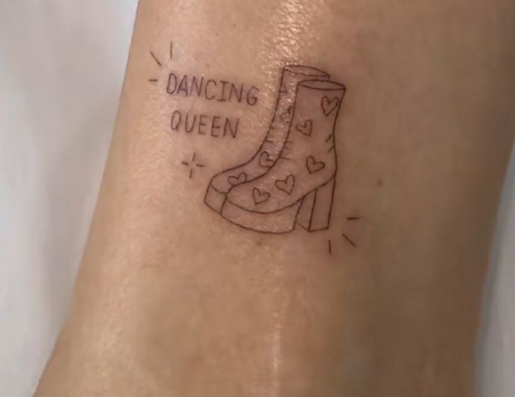 a woman's foot with a tattoo that reads dancing queen and a boot on it