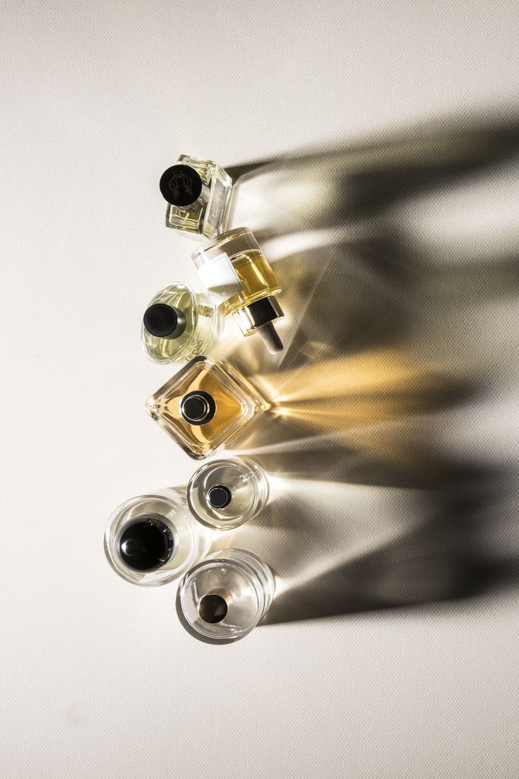 three bottles of perfume sitting next to each other on a white surface with long shadows