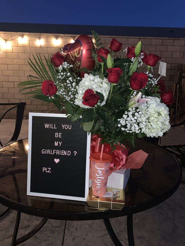 a bouquet of roses and white carnations sits on a table with a sign that says will you be my girlfriend?