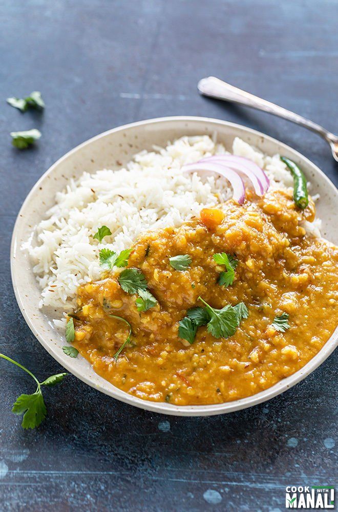 a white bowl filled with rice and curry on top of a blue surface next to a spoon