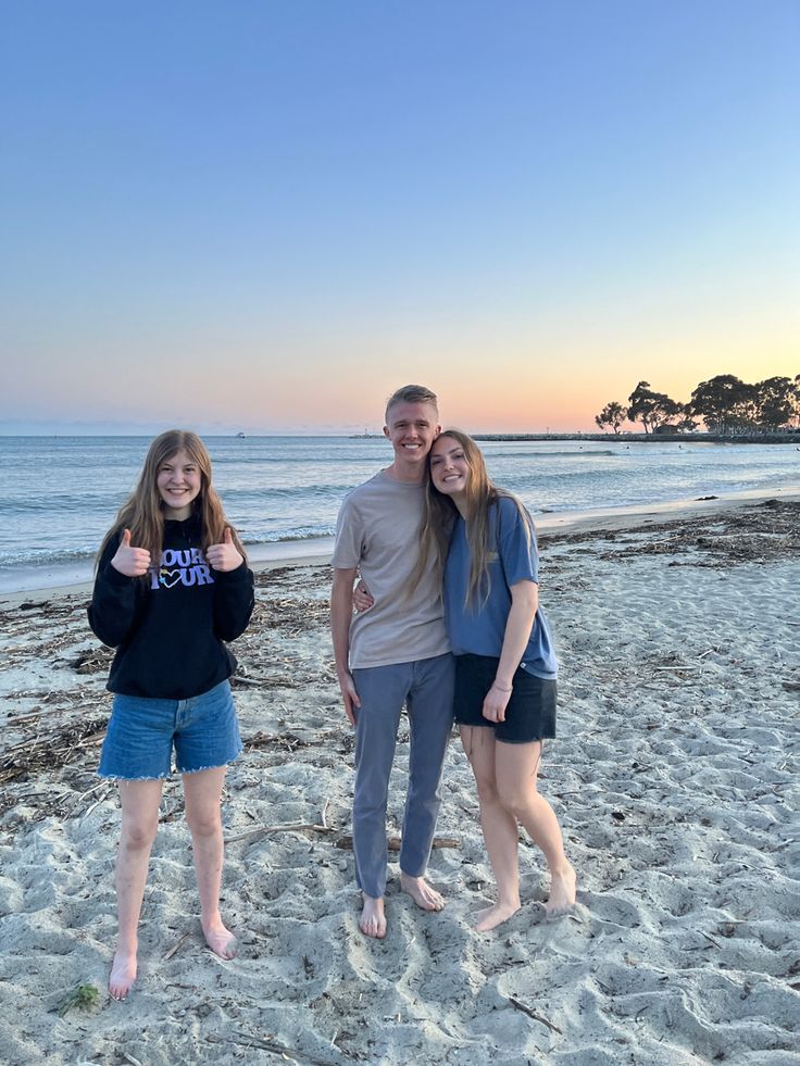 three people standing on the beach with their thumbs up