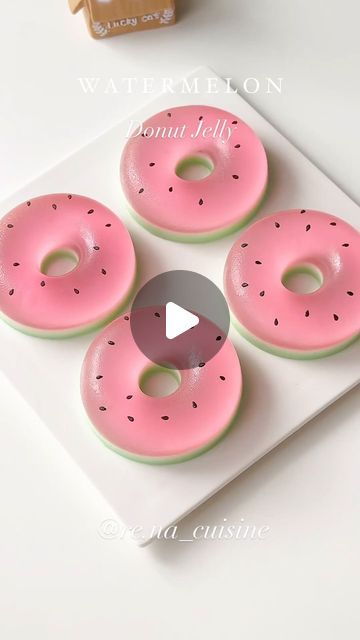 four donuts with pink frosting and sprinkles sitting on a white plate