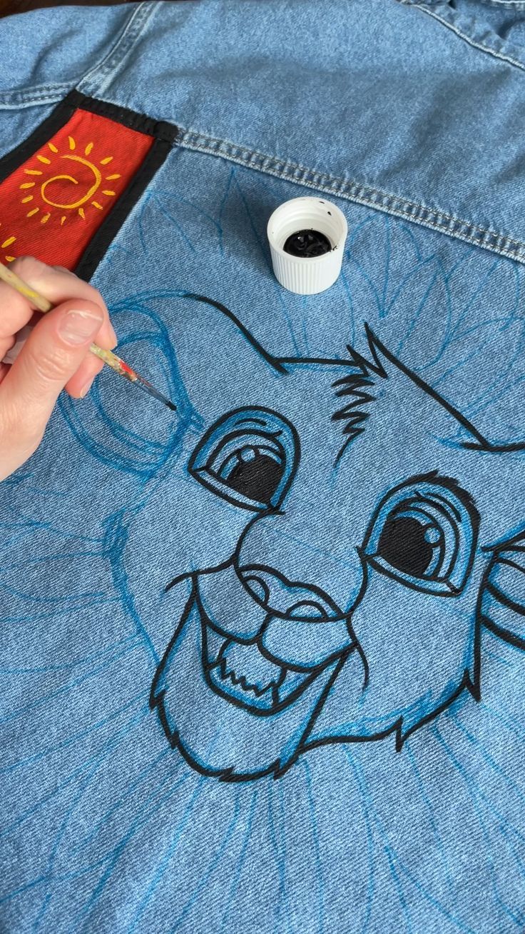 someone is drawing the face of a lion on a jean jacket