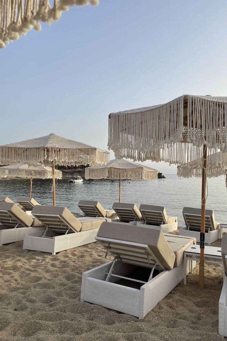 lounge chairs and umbrellas on the beach with water in the backgroung