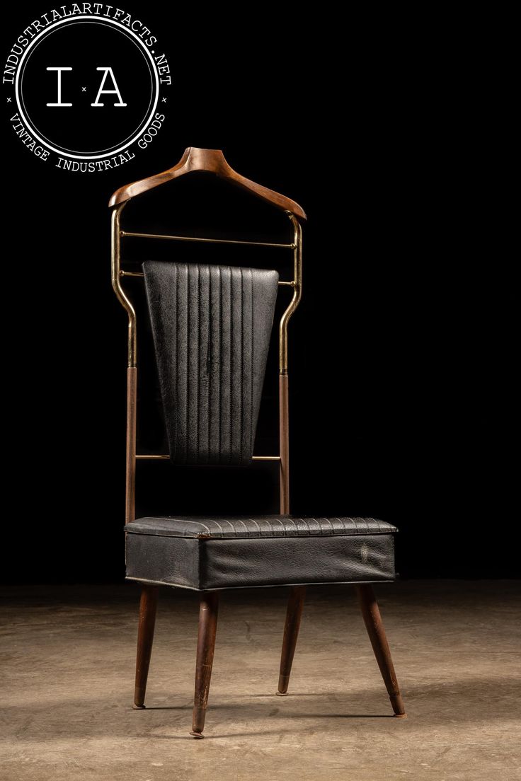 a black leather chair with a wooden frame and backrest, in front of a dark background