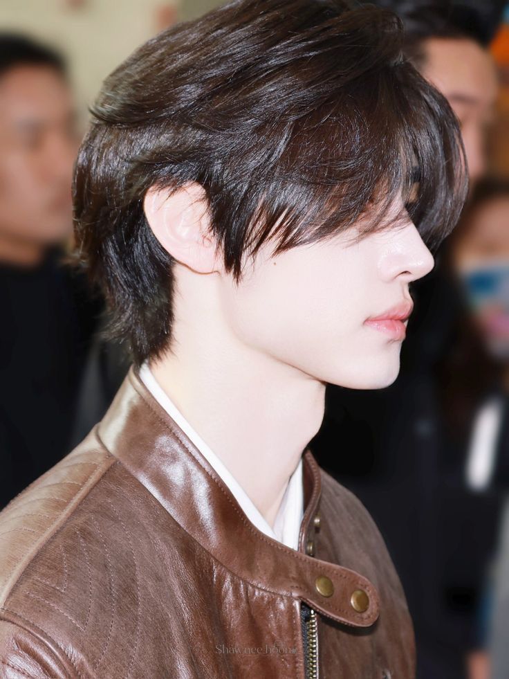 a young man with short hair wearing a brown leather jacket and looking off to the side