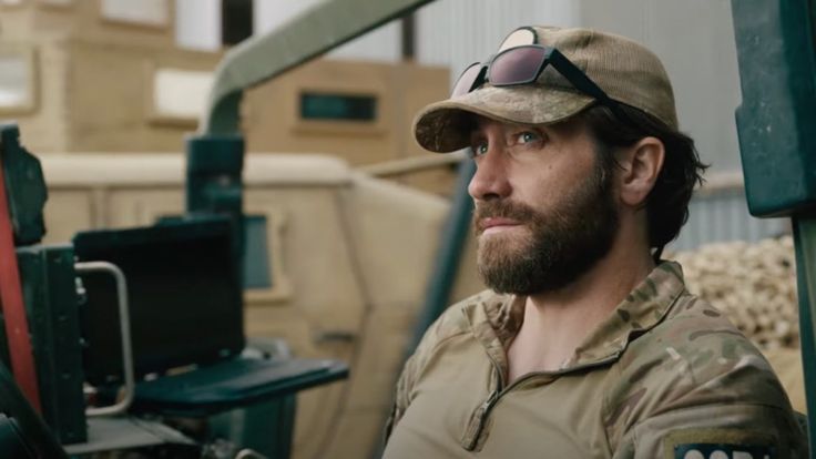 a man wearing a hat and sunglasses sitting in front of a truck with other trucks