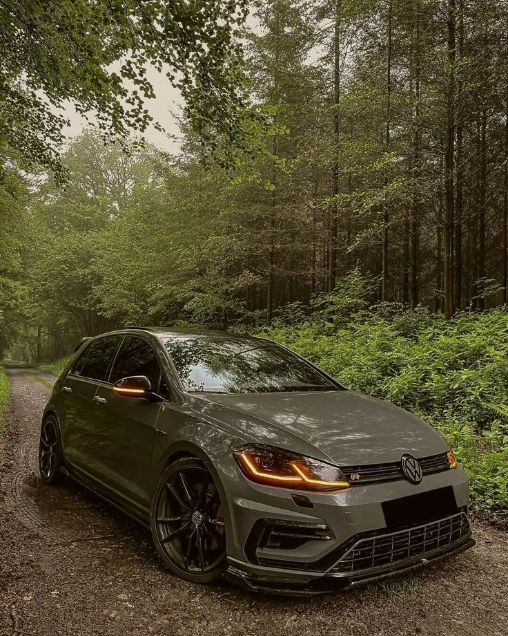 a grey car parked on the side of a dirt road in front of some trees