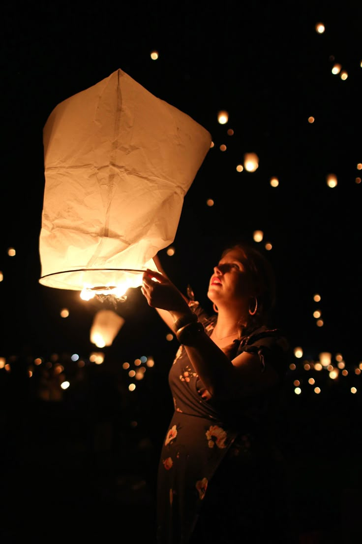 a woman holding up a lantern in the dark with many lights floating around her,