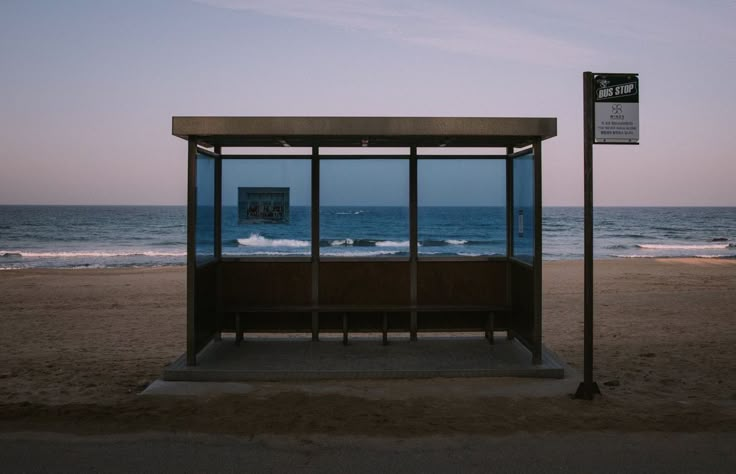 a bus stop sitting on top of a sandy beach next to the ocean at dusk