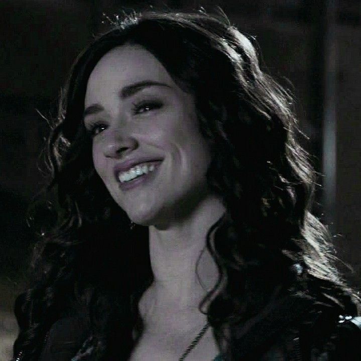 a close up of a person smiling and wearing a black jacket with an open collar