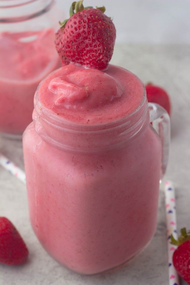 two jars filled with pink smoothie next to strawberries