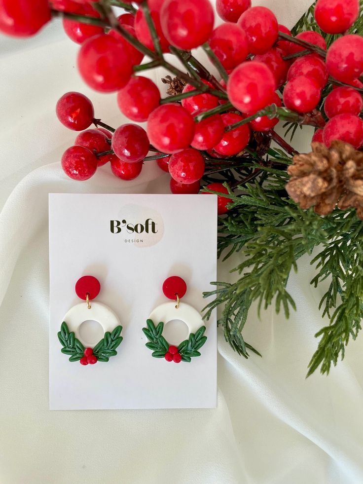 a pair of red and white earrings with holly leaves on them sitting next to berries