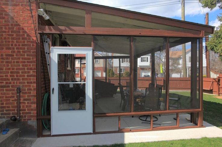 an enclosed patio with sliding glass doors on the front and side of it, next to a brick building