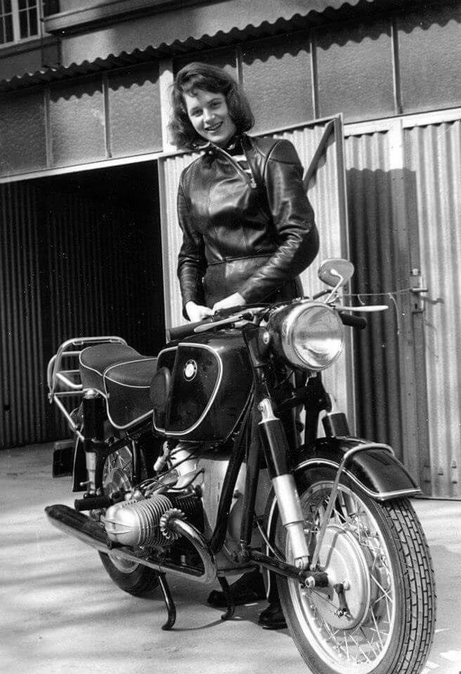 a black and white photo of a woman sitting on a motorbike in front of a building