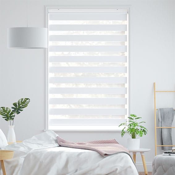 a bedroom with white walls and wooden flooring, windows covered in shades of light