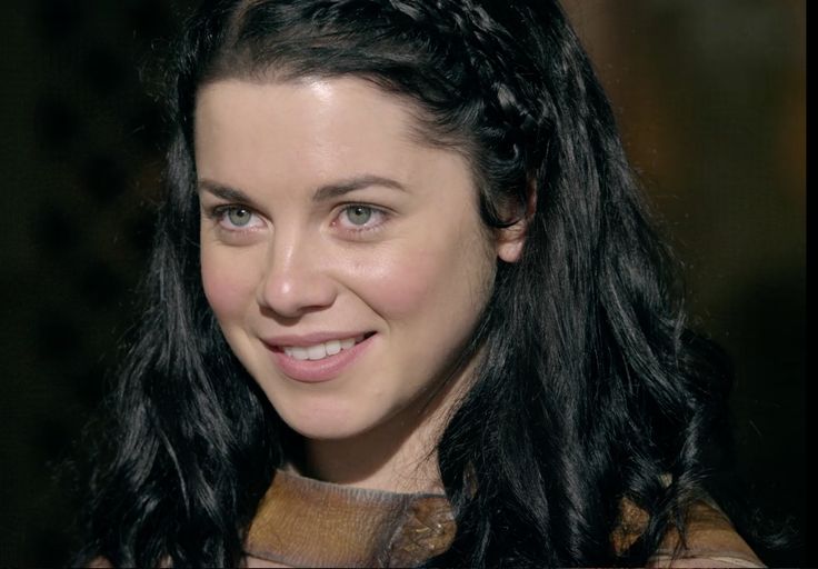 a close up of a person with long hair and wearing a brown dress smiling at the camera