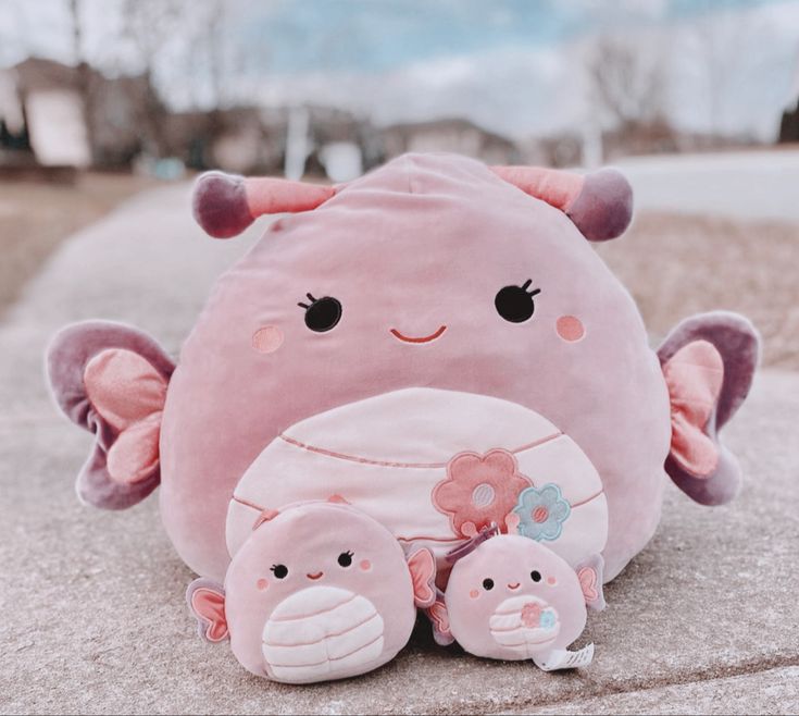 a pink stuffed animal with two smaller ones sitting next to each other on the ground