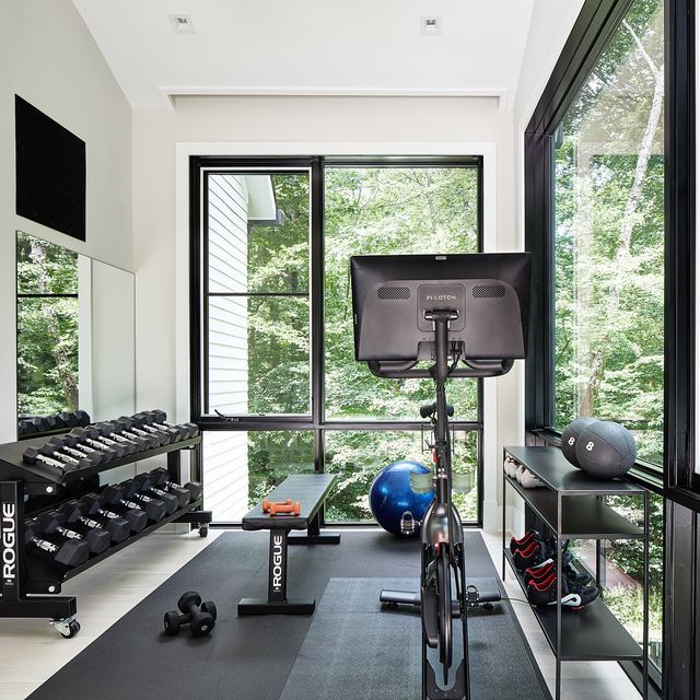 there is a gym with exercise equipment in the room next to the large window that looks out onto the woods