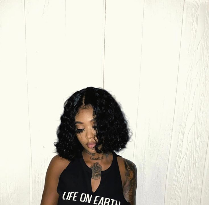 a woman with black hair and tattoos on her chest standing in front of a white wall