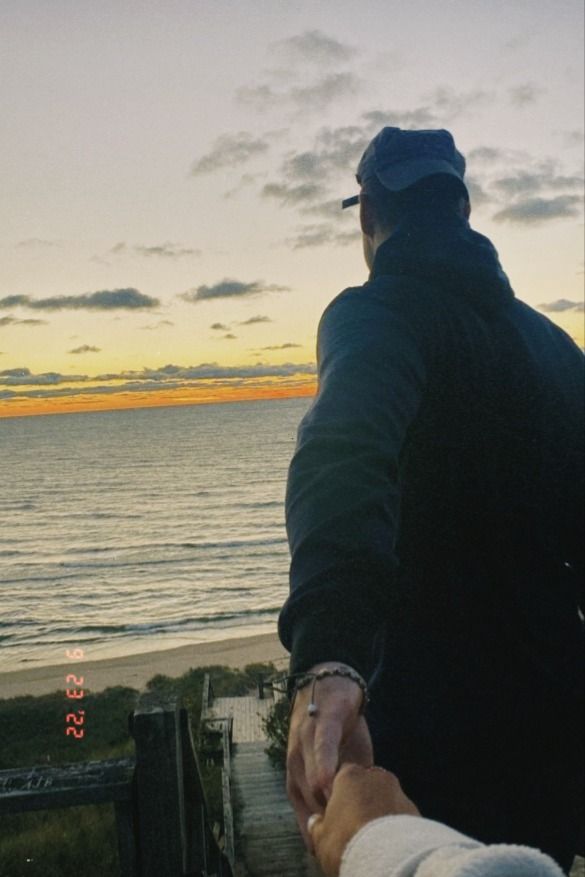 two people holding hands while standing on a boardwalk near the ocean at sunset or dawn