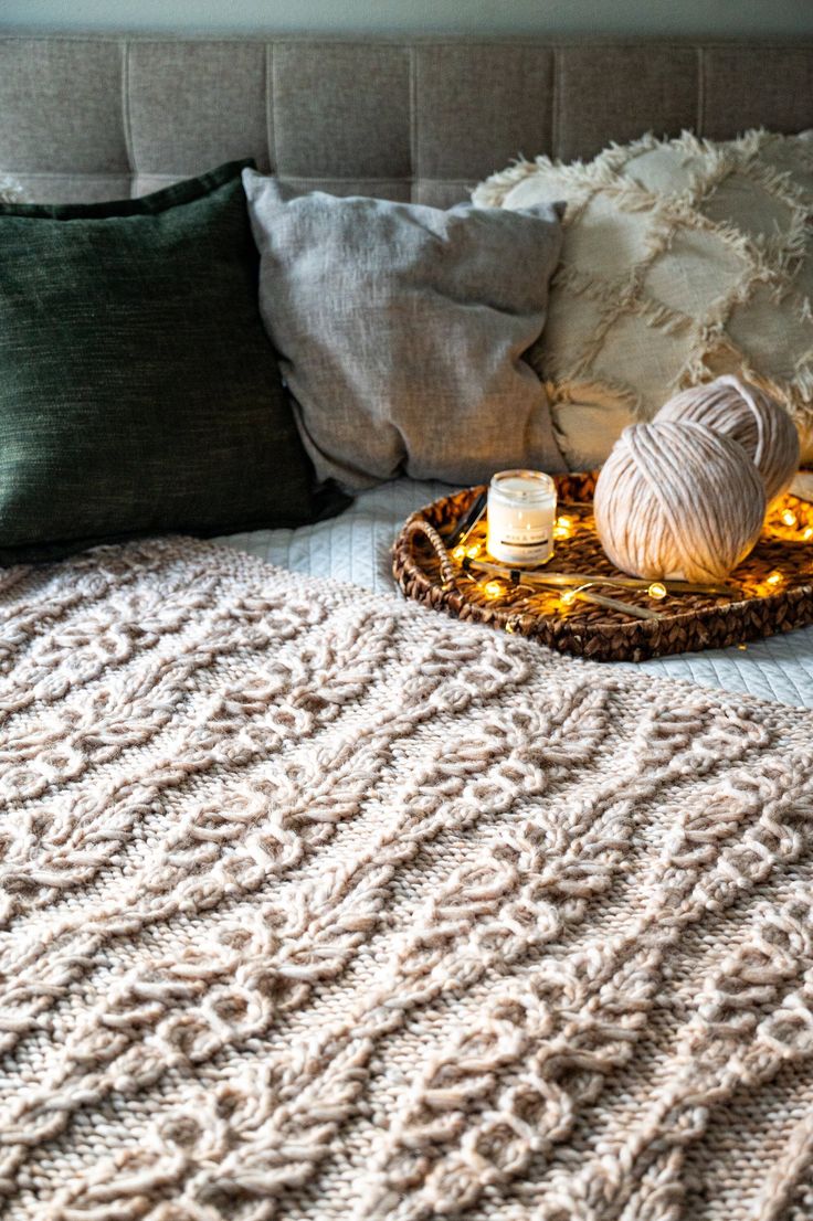 a bed with blankets and pillows on top of it next to a basket filled with balls of yarn