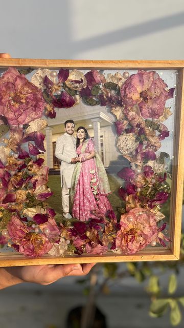 a man and woman are standing in front of flowers holding up an old photo frame