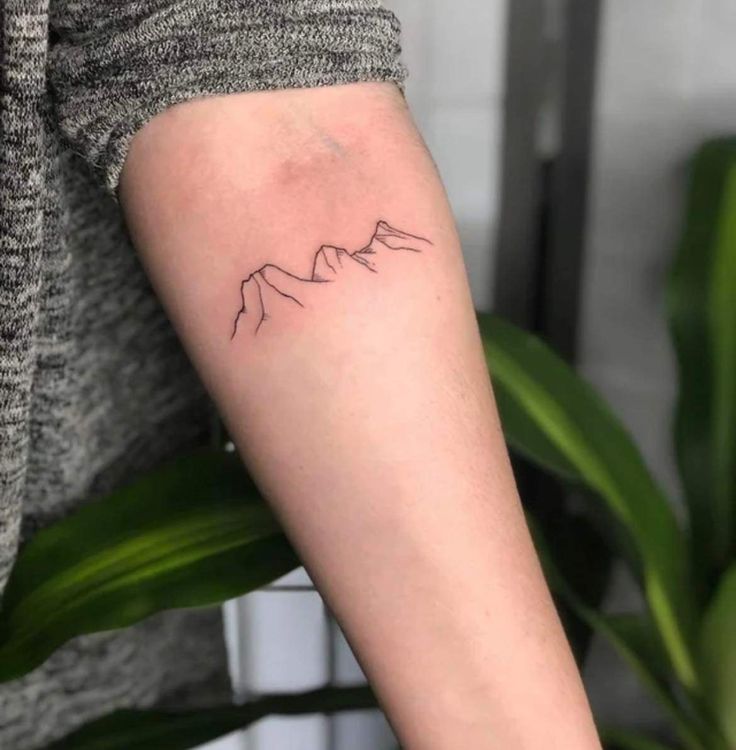 a woman's arm with a small mountain tattoo on the left side of her arm