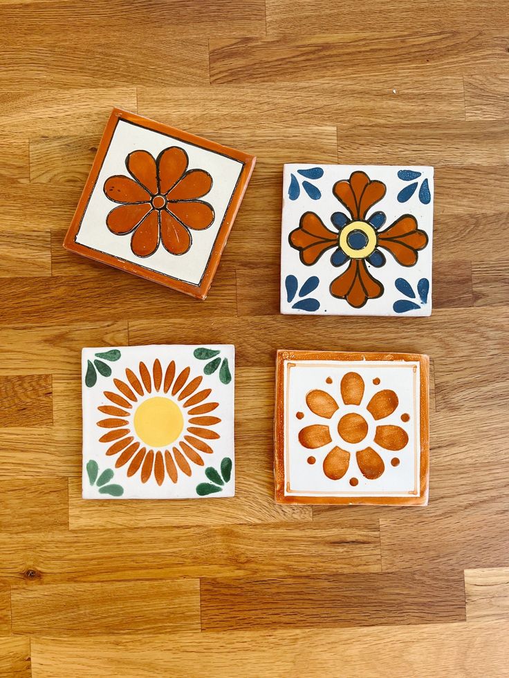 three small ceramic tiles with flowers on them sitting on a wooden floor next to each other