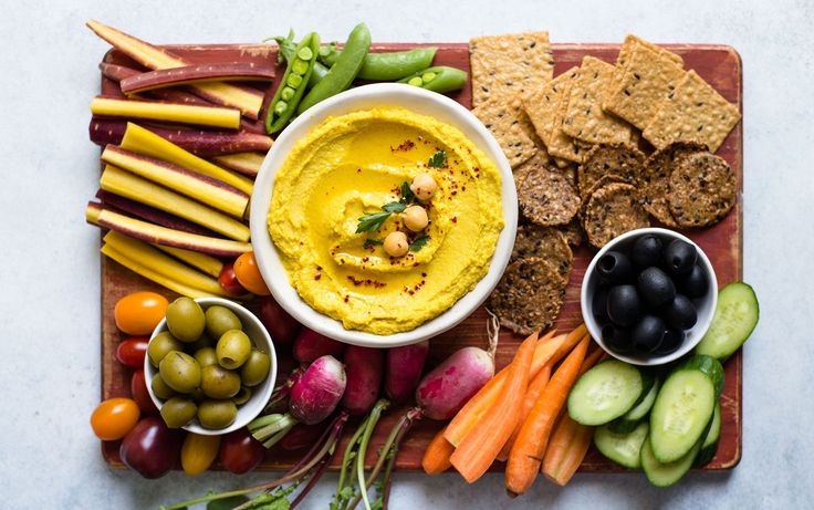 a platter filled with hummus, carrots, celery, radishes, cucumbers and crackers