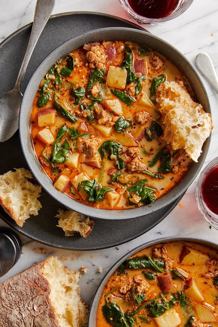 two bowls of stew with bread and wine on the side, next to each other