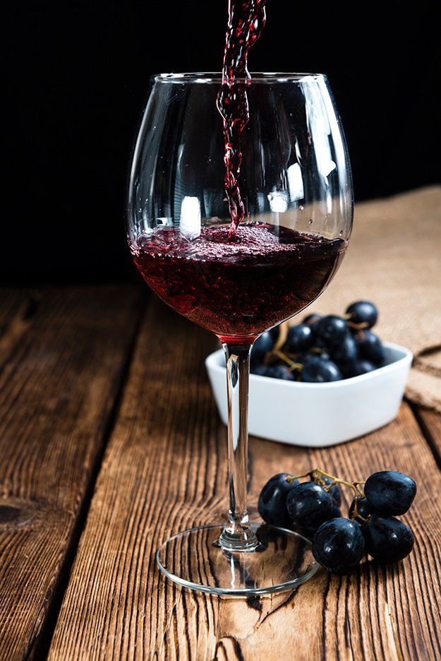 red wine being poured into a glass with black grapes in the foreground on a wooden table