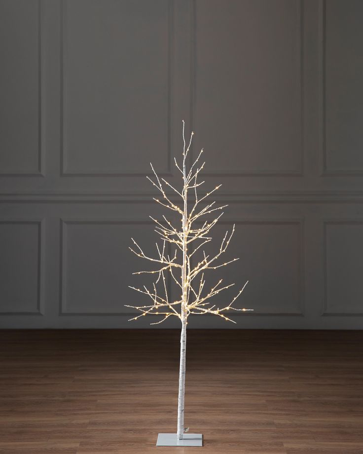 a white christmas tree with lights on it in front of a gray wall and wooden floor