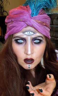 a woman with blue eyes and black makeup is wearing a pink turban hat