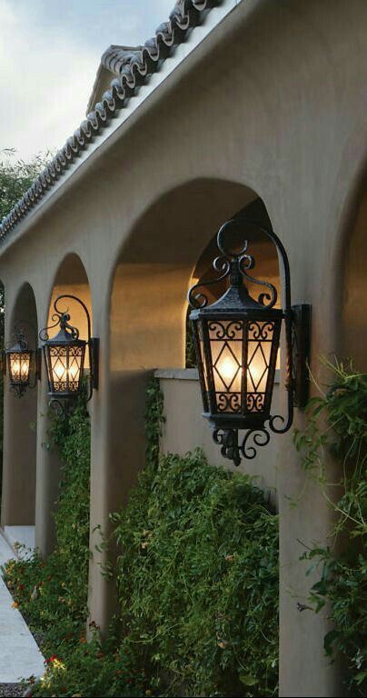 two lamps are on the side of a building near some bushes and trees in front of it