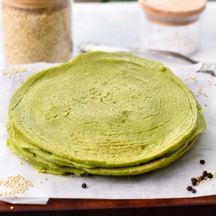 a stack of green pancakes sitting on top of a wooden table next to some spices