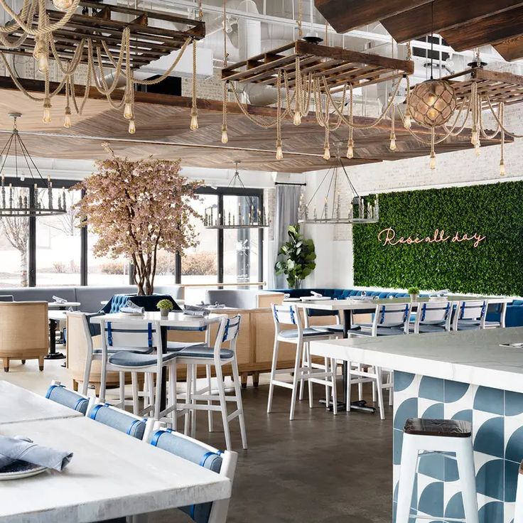 the interior of a restaurant with blue and white tables, chairs, and plants on the wall