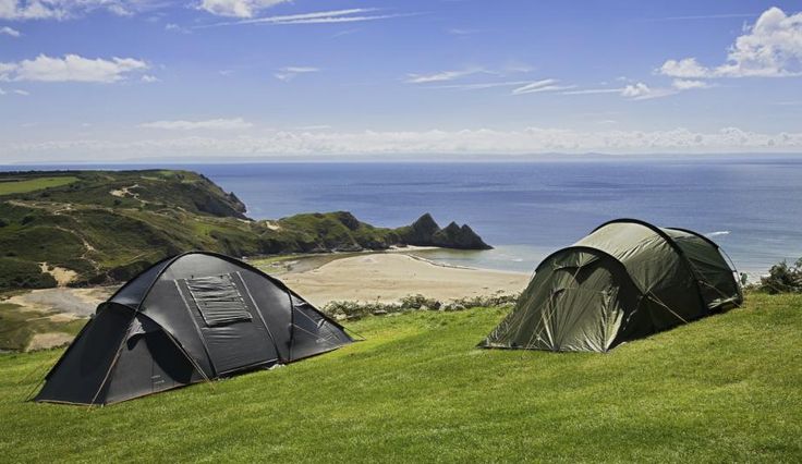 two tents set up in the grass on top of a hill next to the ocean