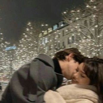 a man and woman kissing in front of a city street with christmas lights on the trees