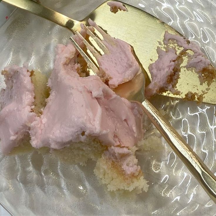 a piece of cake with pink frosting on a plate next to a gold fork