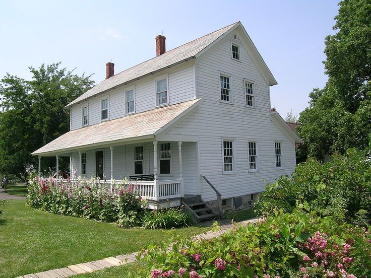 a large white house sitting in the middle of a lush green field with lots of flowers