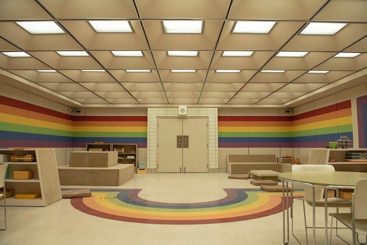 an empty room with tables, chairs and a rainbow rug on the floor in front of it