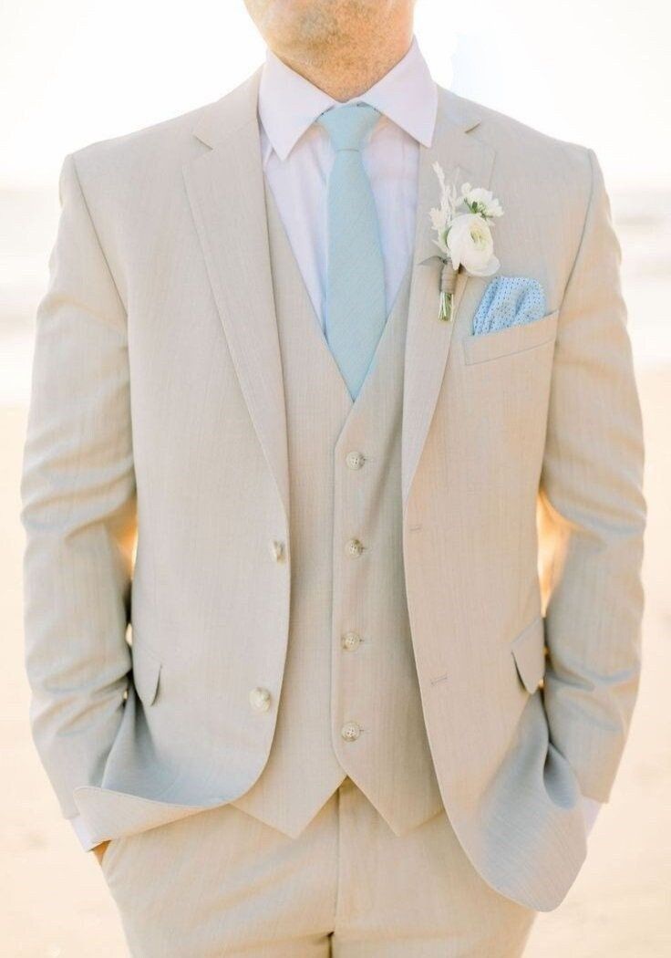 a man in a suit and tie standing on the beach with his hands in his pockets