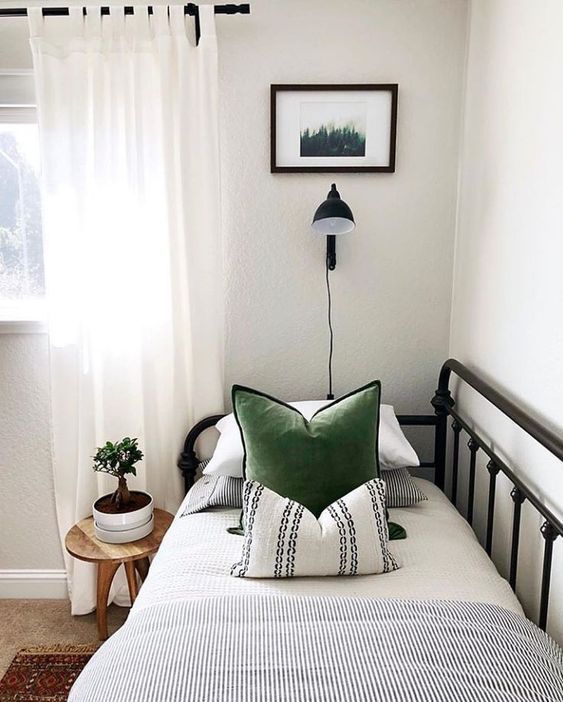 a bed with white sheets and green pillows in a small room next to a window