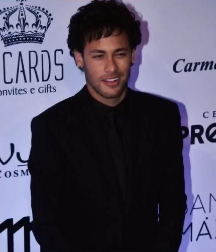 a man standing in front of a white wall wearing a black suit and smiling at the camera