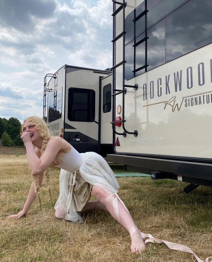 a woman sitting on the ground in front of a white bus with her legs crossed