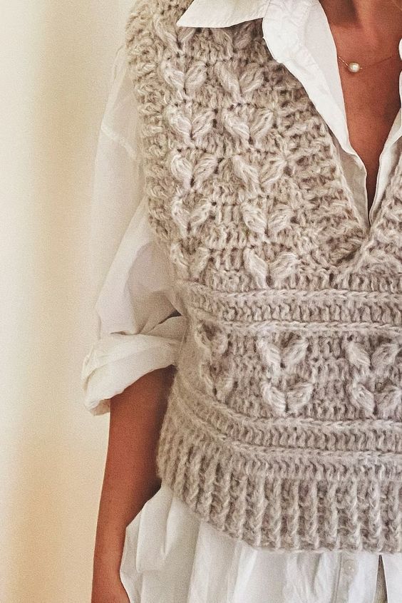 a woman wearing a crocheted vest and white shirt