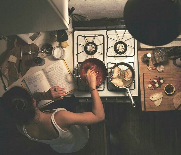 a woman is reading a book while cooking in the kitchen