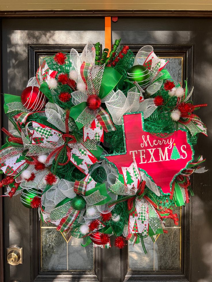 a christmas wreath on the front door of a house that says merry texas with green, red and white decorations